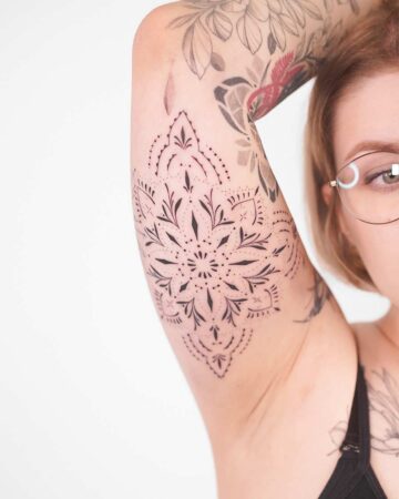 A sharp, high-contrast mandala tattoo on the inner bicep, showcasing perfectly symmetrical patterns and fine-line decorative edges.