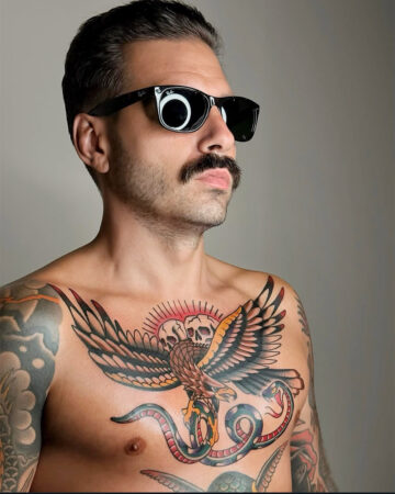 A man with a mustache and sunglasses showcases a vibrant color traditional tattoo of an eagle and snake on his chest. Created in the multi style tattoo studio in Canggu Bali, a top destination for Bali tattoo artists.