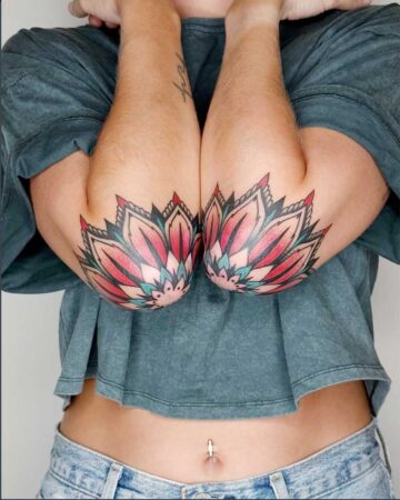 Two vibrant, color tattoos of lotus flowers adorn the inner elbows of a person, showcasing intricate details and a blend of pink, red, and teal hues. Created in the multi style tattoo studio in Canggu Bali.