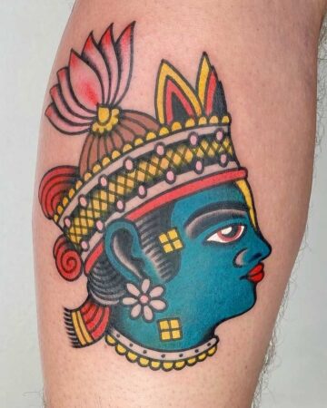 Vibrant color traditional tattoo of a blue-faced deity with a red eye, adorned with a golden crown and a pink lotus flower. Created in the multi style tattoo studio in Canggu Bali, Bali tattoo studio, best tattoo in Canggu.