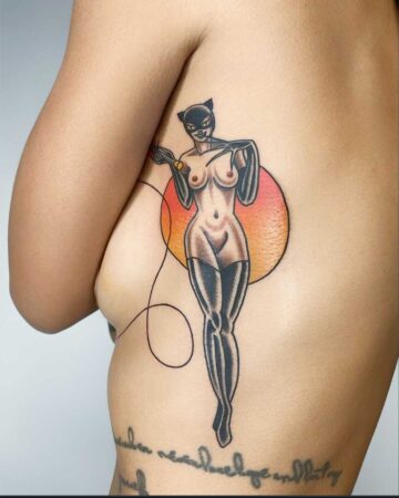 Color traditional tattoo of Catwoman with black mask and whip, against a vibrant orange circle. Bali tattoo studio.