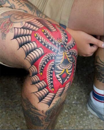 Vibrant color traditional tattoo of a spider and web covering a knee, showcasing bold red, yellow, and black ink. Created in the multi style tattoo studio in Canggu Bali.