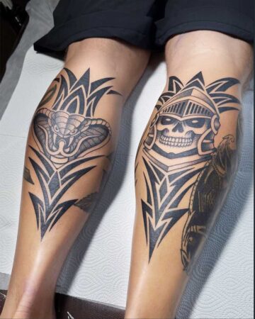 Close-up of two black and grey tribal-style leg tattoos: a cobra on the left and a skull in a helmet on the right. Created in the multi style tattoo studio in Canggu Bali, a top Bali tattoo destination.