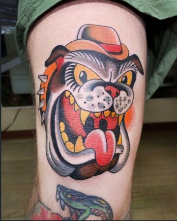 A vibrant, color traditional tattoo of a fierce bulldog wearing a hat. This bold tattoo design showcases intense eyes, a wide grin with sharp teeth, and a bright red tongue. Created in the multi style tattoo studio in Canggu Bali for an unforgettable Bali tattoo experience.