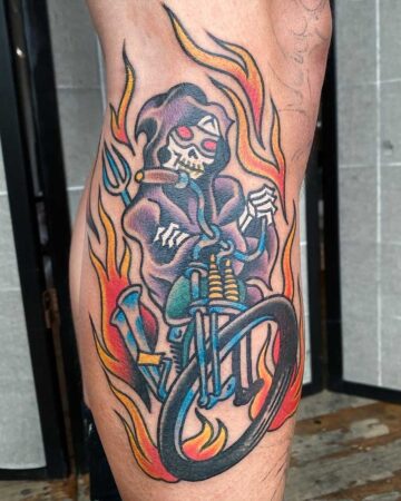 Vibrant color traditional tattoo of the Grim Reaper riding a motorcycle through flames, holding a cigar and trident. Bali tattoo studio.