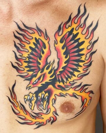 Vibrant color traditional tattoo of a phoenix with fiery wings spread across a chest. The bold red, yellow, and black ink depicts the mythical bird rising from flames, a powerful symbol of rebirth. Bali tattoo studio Canggu.