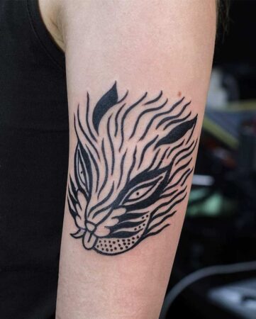 Close-up of a bold, black ink tiger tattoo on an arm. The minimalist design features stylized lines and dots. A unique tiger tattoo design. Bali tattoo artist.