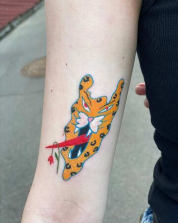 Close-up of a vibrant tiger tattoo on an arm, featuring a unique design with a flower in its mouth. A striking tiger tattoo design. Created by the best tattoo artists in Canggu Bali for your next Bali tattoo.