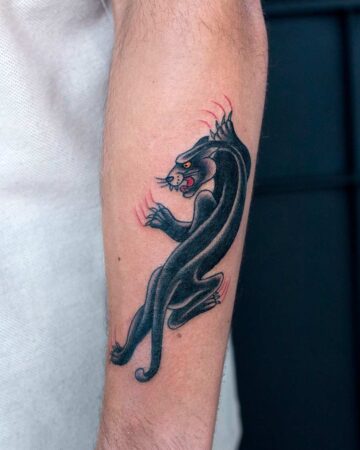 classic Traditional tattoo of a black panther with red claws on a person's forearm. The panther is posed dynamically, with sharp details and bold outlines.