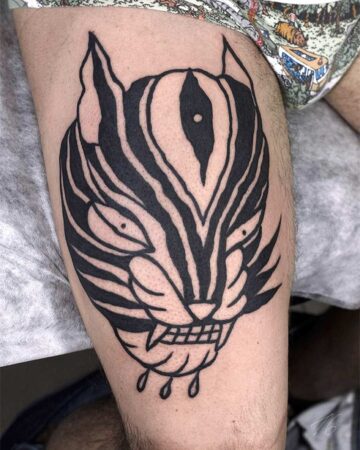 Bold black ink tiger tattoo on a person's thigh. Striking traditional tiger tattoo design. Bali tattoo artist.