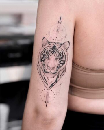 Upper arm tattoo of a tiger's face with geometric shapes, showcased in a gallery of cat-themed designs like a lion tattoo. The black ink design features intricate line work.