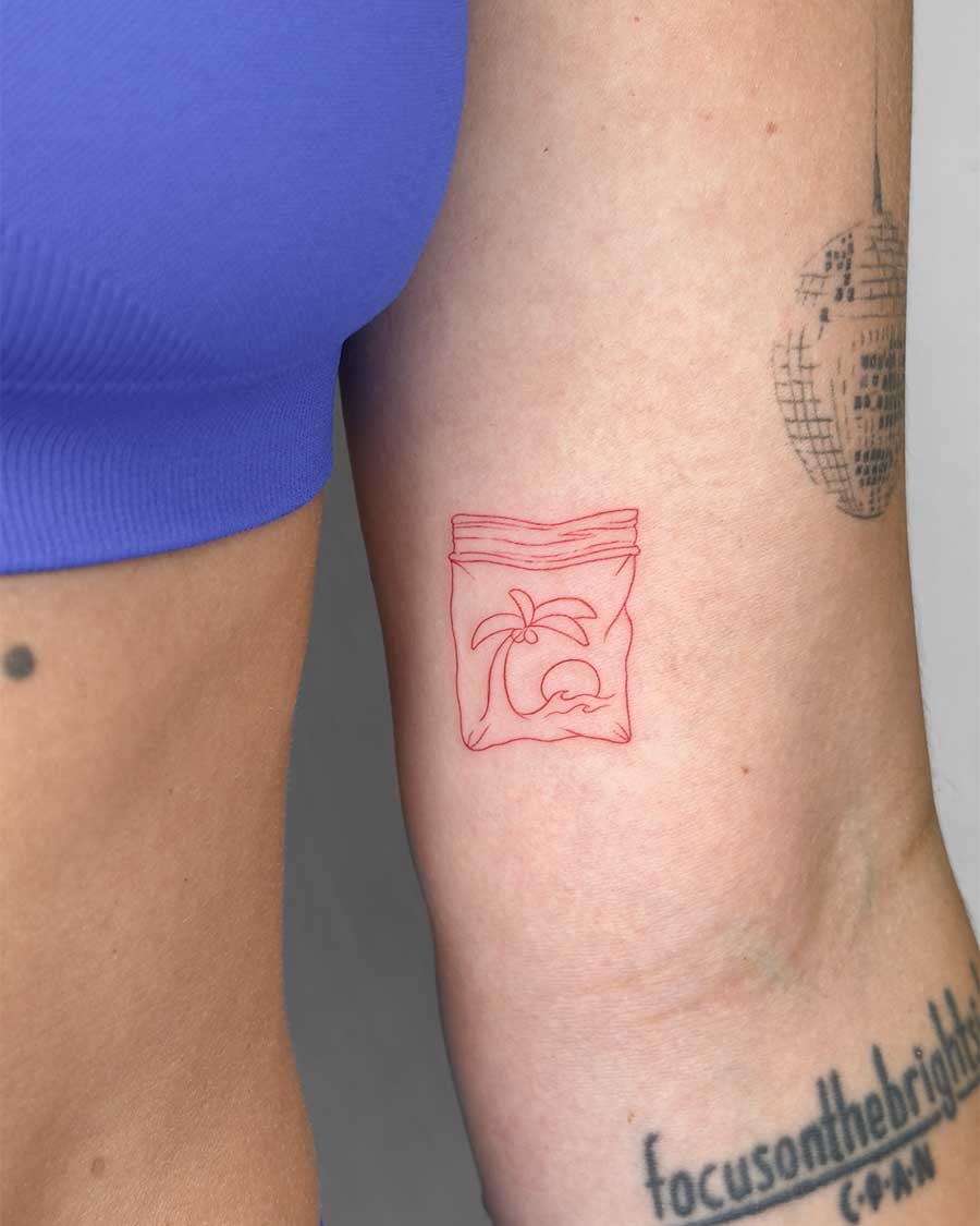 A minimalist red line tattoo of a palm tree and waves inside a plastic bag on an arm. Created in the FLT Tattoo, a multi-style tattoo studio in Canggu, Bali, offering unique Bali tattoo designs.