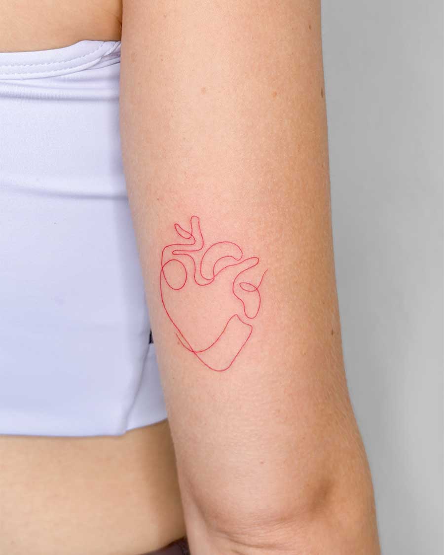 A minimalist red line tattoo of a human heart on a person's arm. Created in the FLT Tattoo, a multi-style tattoo studio in Canggu, Bali, offering unique Bali tattoo artistry.