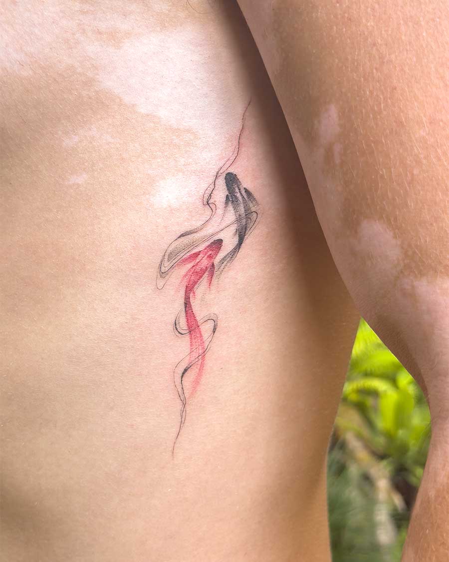 Delicate red and black koi fish tattoo on a person's side, symbolizing balance and duality. Created in the FLT Tattoo, a multi-style tattoo studio in Canggu, Bali, offering unique Bali tattoo artistry.