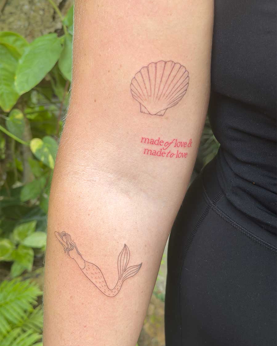 Red ink tattoo of a seashell and a mermaid on a person's arm, with red script reading "made of love & made to love." Created in the "FLT Tattoo" a multi style tattoo studio in Canggu, Bali.
