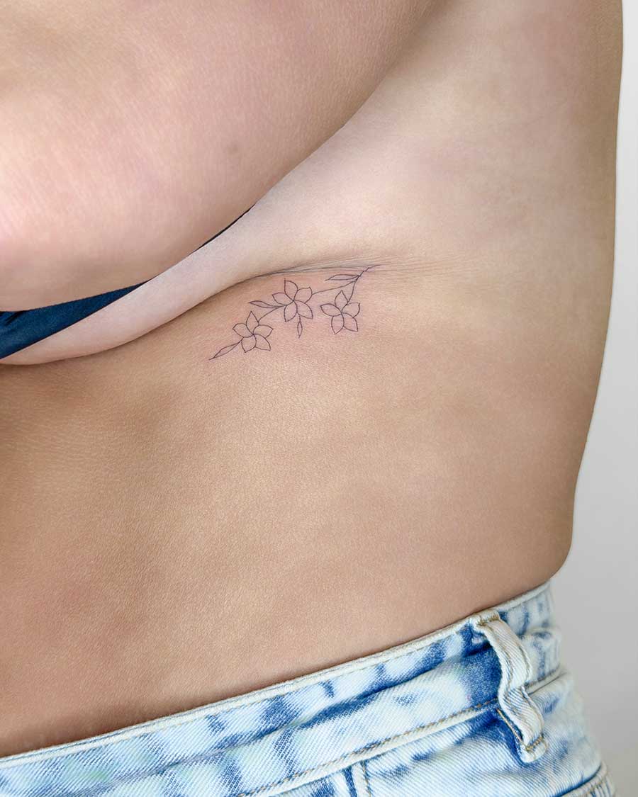 Delicate line art tattoo of three frangipani flowers on a woman's torso. Created in the multi style tattoo studio in Canggu Bali.