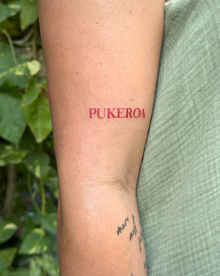 Close-up of a person's arm showcasing a bold, red tattoo spelling "PUKEROA" in uppercase letters. Created in the FLT Tattoo, a multi-style tattoo studio in Canggu, Bali, for your Bali tattoo needs.