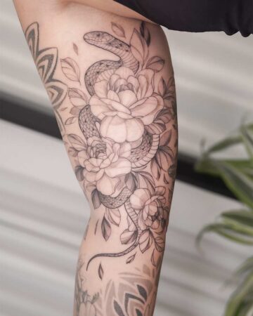 Elegant arm tattoo featuring a snake coiled around blooming roses, rendered in delicate linework. The floral and reptile design creates a striking contrast on the skin. Created by our tattoo artists in Canggu, Bali