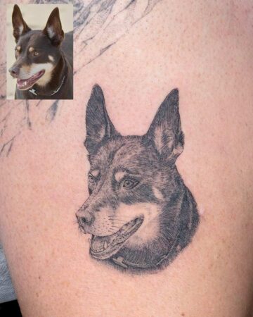 A striking micro realism tattoo of a dog's head, closely resembling the reference photo inset. The black and grey ink captures the dog's expressive face and detailed fur texture.