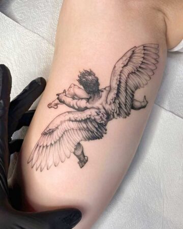 Close-up of a micro realism tattoo on an arm, featuring a detailed cherub with large wings, rendered in fine lines and stippling. This example showcases the artistry of micro realism tattoo techniques. Done by our expert tattoo artists at our fine line tattoo studio in Canggu, Bali.