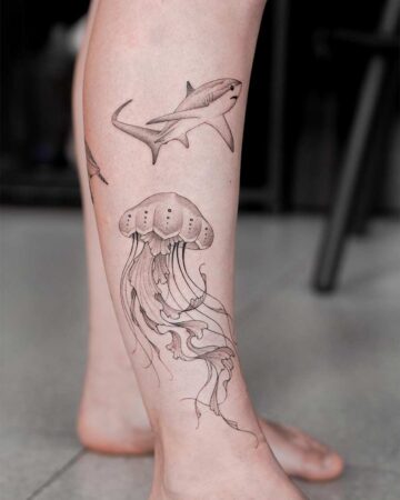 Leg tattoo featuring a shark and jellyfish. This marine life tattoo showcases intricate line work and shading, capturing the beauty of aquatic creatures.