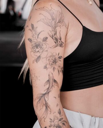 Close-up of a woman's arm featuring an aquatic creatures tattoo with koi fish swimming amongst delicate peony flowers in a black ink design.