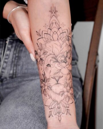 Detailed line art tattoo of a lion's face adorned with flowers and geometric mandala elements on a woman's forearm. A striking example for a tiger Tattoos gallery.