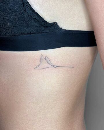 Minimalist marine life tattoo of a stingray on a woman's ribcage, showcasing delicate linework. A simple yet elegant aquatic creature design.