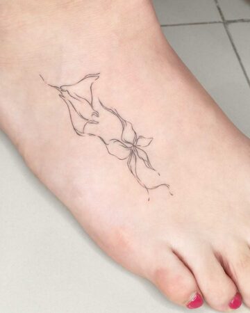 Delicate fine-line tattoo of a stylized aquatic creature or marine life form on a woman's foot. The minimalist design features flowing lines and abstract shapes. Created by our tattoo artists in Canggu, Bali