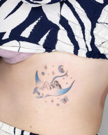 A whimsical marine life tattoo of a woman reclining on a manta ray, surrounded by stars, a crescent moon, and a butterfly. A unique aquatic creature design.