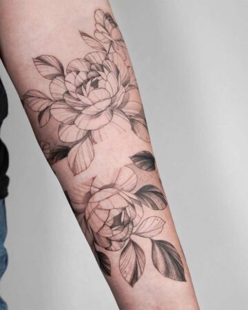 Elegant peony tattoo design on a forearm. Two large, detailed floral tattoos with shading and line work create a striking botanical art piece.