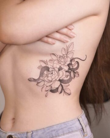 A delicate snake tattoo winds through blooming peonies on a woman's ribcage. This elegant body art combines the symbolism of the snake tattoo with the beauty of floral design.