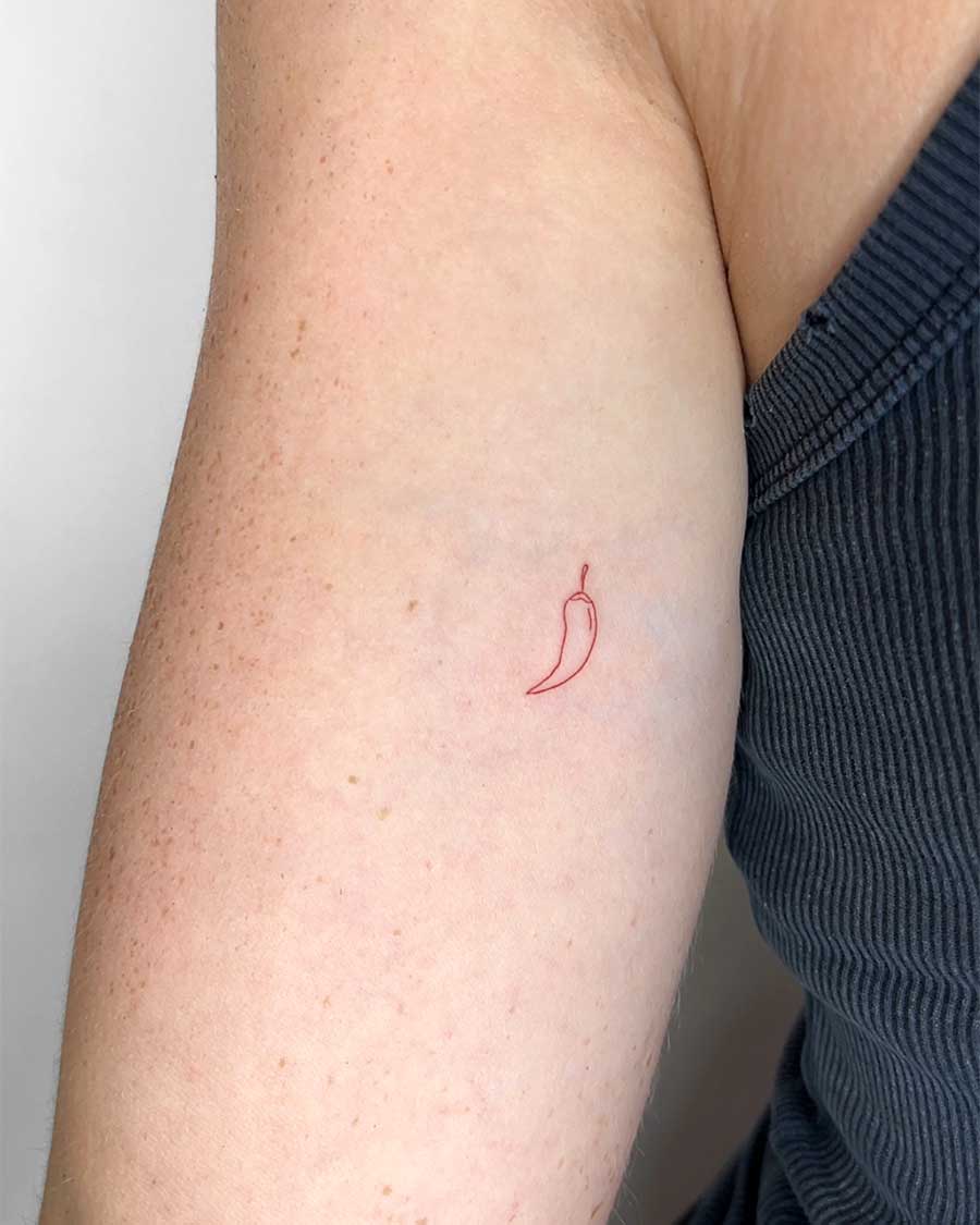 A minimalist red chili pepper tattoo inked in red outline on a person's upper arm. Created in the FLT Tattoo, a multi-style tattoo studio in Canggu, Bali, known for its Bali tattoo artistry.