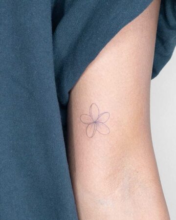 Close up of a delicate frangipani plumeria tattoo in simple line art on a person's upper arm. A subtle and elegant floral design.