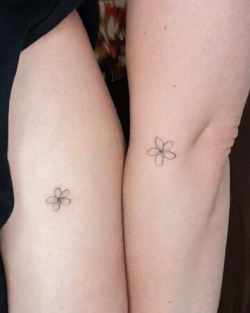 Two arms display delicate, minimalist Frangipani Plumeria flower tattoos. The simple line work captures the beauty of the bloom. A subtle and elegant Frangipani Plumeria tattoo design.