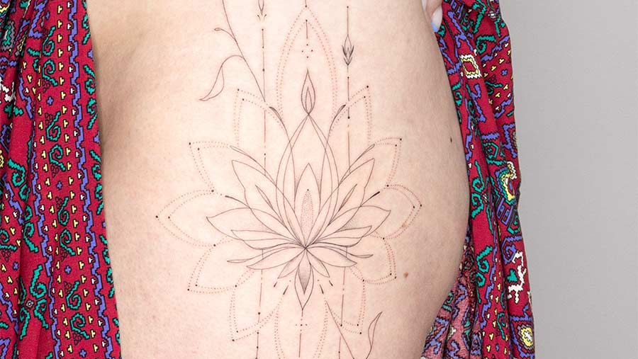 Close-up of a delicate lotus flower tattoo on a woman's side, featuring fine line work and dot shading, accented by a colorful patterned robe. A beautiful example of lotus flower tattoo art.