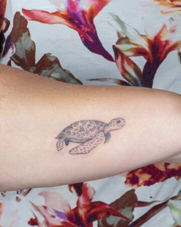 Close-up of a delicate, fine-line marine life tattoo of a sea turtle on a person's arm, set against a colorful floral background.