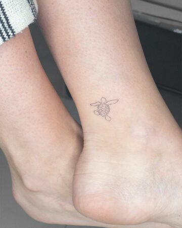 Delicate, minimalist fine-line tattoo of a sea turtle on a woman's ankle. A subtle aquatic creature design for marine life tattoo inspiration. Created by our tattoo artists in Canggu, Bali
