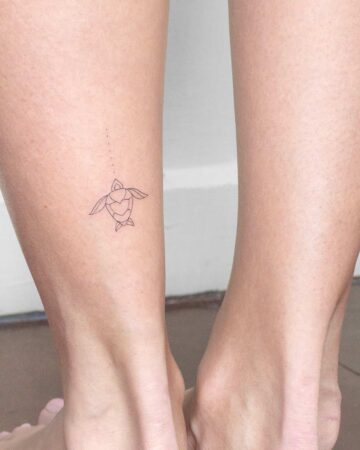 Delicate fine-line turtle tattoo on a person's lower leg. This aquatic creature tattoo features a minimalist design, with a geometric shell and small dots trailing upwards. Created by our tattoo artists in Canggu, Bali