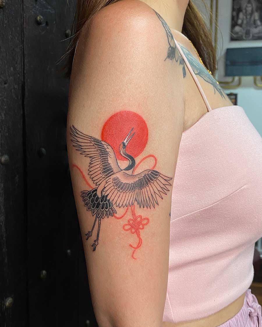 Arm tattoo featuring a Japanese crane in flight against a red sun, with a decorative knot. This Japanese tattoo design is a stunning example from our Japan tattoo gallery. Created in the multi style tattoo studio in Canggu Bali