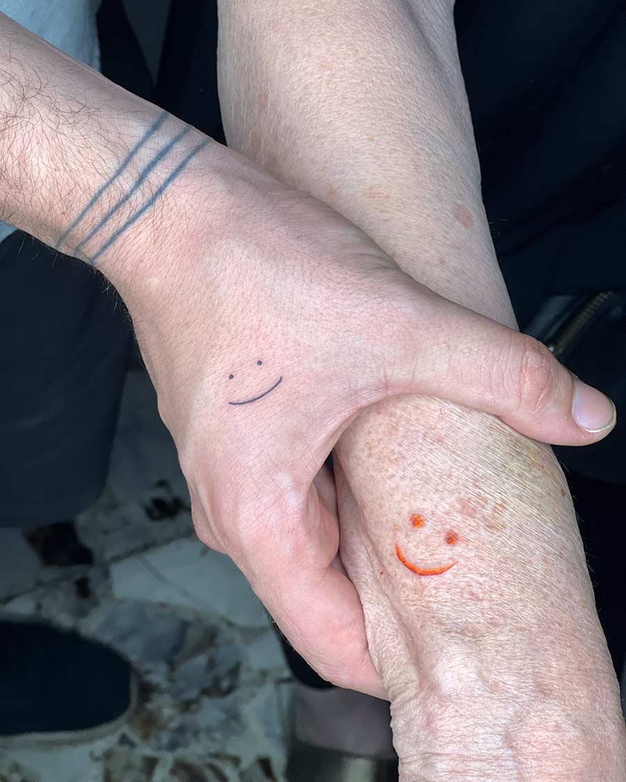 Two hands clasped together, showcasing matching tattoos of simple smiley faces. A sweet example of family matching tattoos, symbolizing connection and shared joy. Created by expert tattoo artists in Bali.