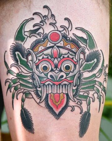 A vibrant Barong tattoo design featuring a crab-like creature with a traditional Balinese mask face. The tattoo incorporates green, red, gold, and gray colors. Created by expert tattoo artists in Canggu, Bali.