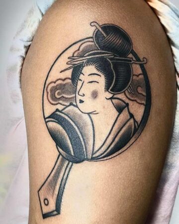 A striking Japanese tattoo on an arm, depicting a Geisha in a hand mirror against a cloudy sky. A beautiful piece from our Japanese & Oriental tattoo gallery. Created in a multi-style tattoo studio in Canggu, Bali. Bali tattoo design.