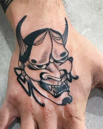 Close-up of a bold, black ink Hannya mask tattoo on a hand. This Japanese-inspired design showcases sharp lines and shading. Created in the multi style tattoo studio in Canggu Bali.