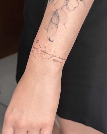 Wrist with a delicate "sun always rises" bracelet tattoo. The minimalist design features a sun, moon, and stars. Bali tattoo art.