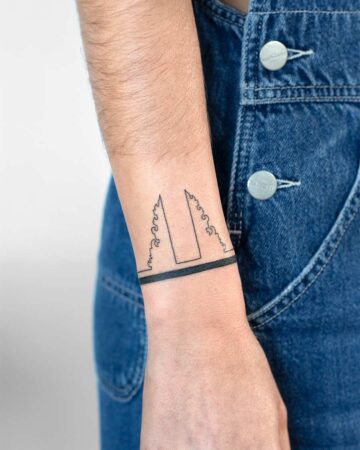 Wrist tattoo of a bracelet design featuring a gate and wave-like elements. This bracelet tattoo embodies Bali's artistic spirit. Created by expert tattoo artists in Canggu, Bali.