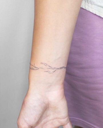 Wrist with a delicate, minimalist line art bracelet tattoo. The subtle design wraps around the wrist. Created by the best expert tattoo artists in Canggu Bali.