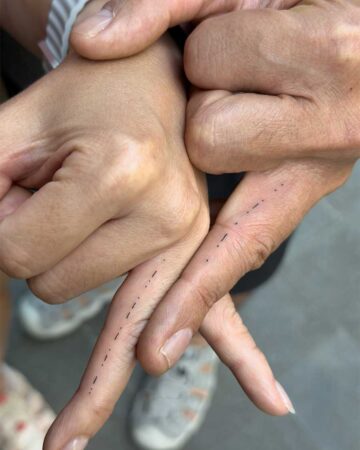 Matching abstract finger tattoos on two hands. The design consists of varying thicknesses of vertical black parallel lines of different lengths, creating morse code on the ring fingers.