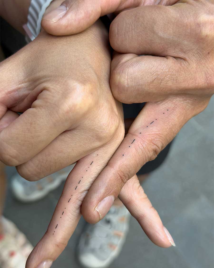 Matching abstract finger tattoos on two hands. The design consists of varying thicknesses of vertical black parallel lines of different lengths, creating morse code on the ring fingers.