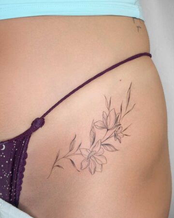 Delicate floral tattoo on hip, featuring a minimalist line drawing of blooming flowers and leaves. Created in a multi-style tattoo studio in Canggu, Bali, offering unique Bali tattoo artistry.